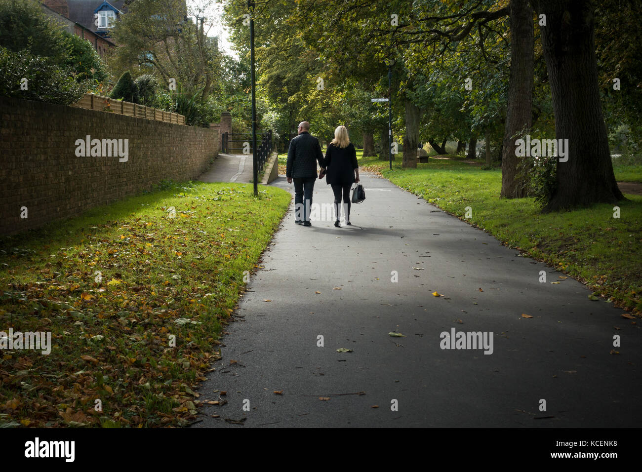 Mature couple, holding hands, stroll together along quiet, scenic, tree-lined, riverside footpath in early autumn - New Walk path, York, England, UK. Stock Photo