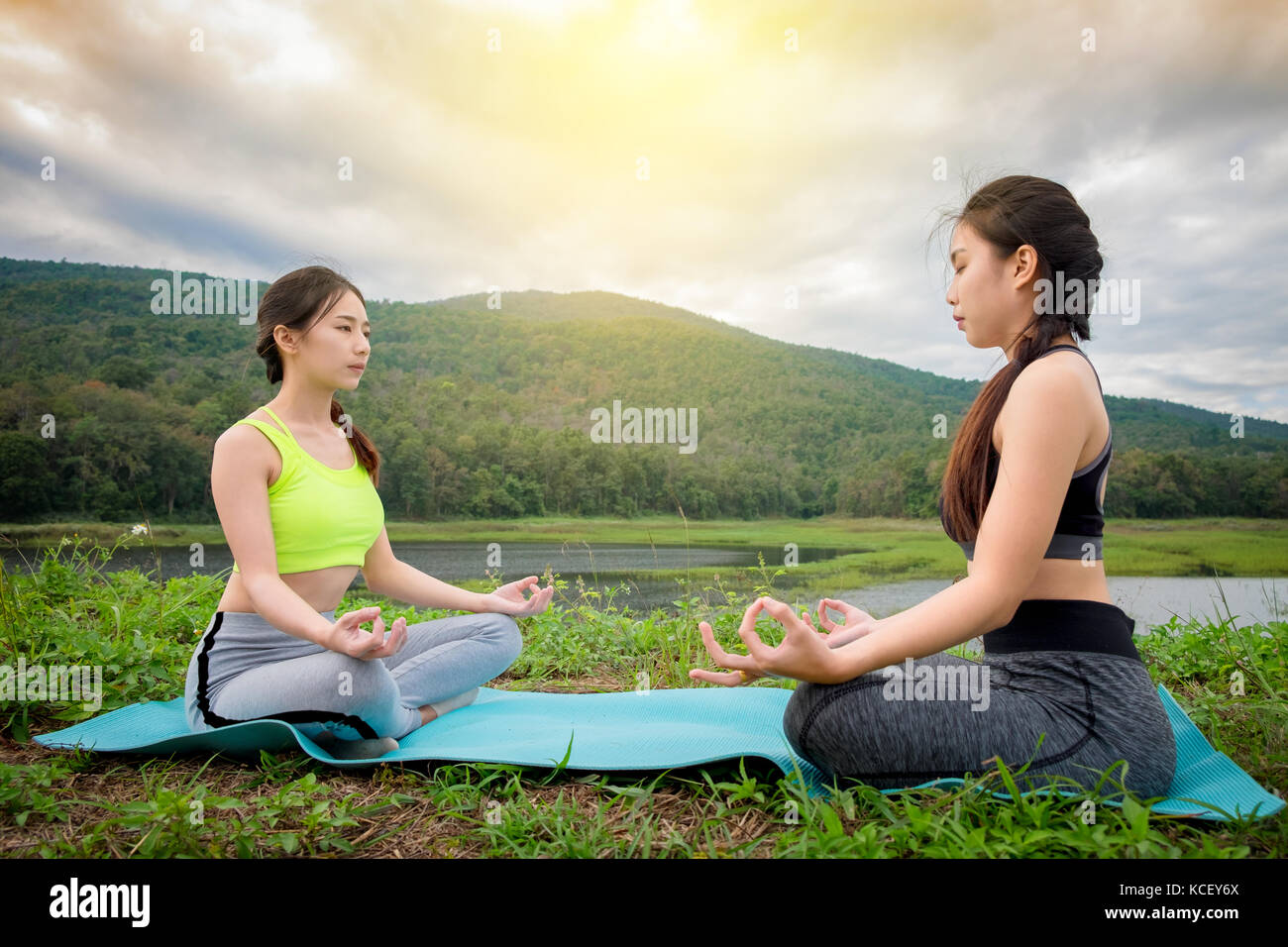 Two young womans sitting Yoga near river. Concept of healthy lifestyle and relaxation. Stock Photo