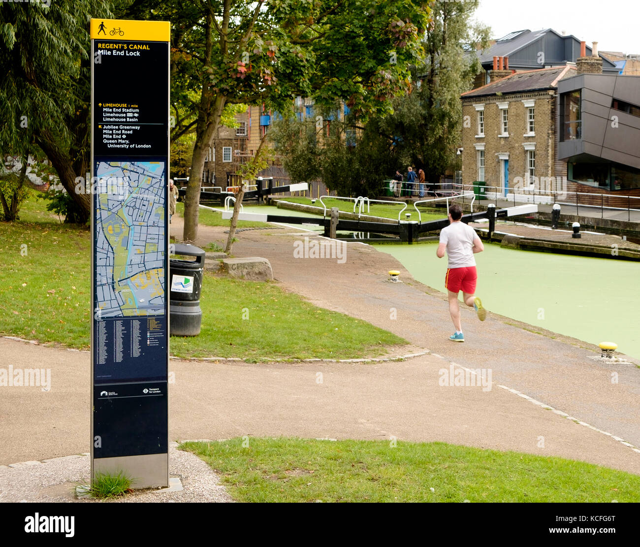 A jogger runs on the towpath passing a Legible London column street sign at Mile End Lock on the Regents Canal, London Stock Photo