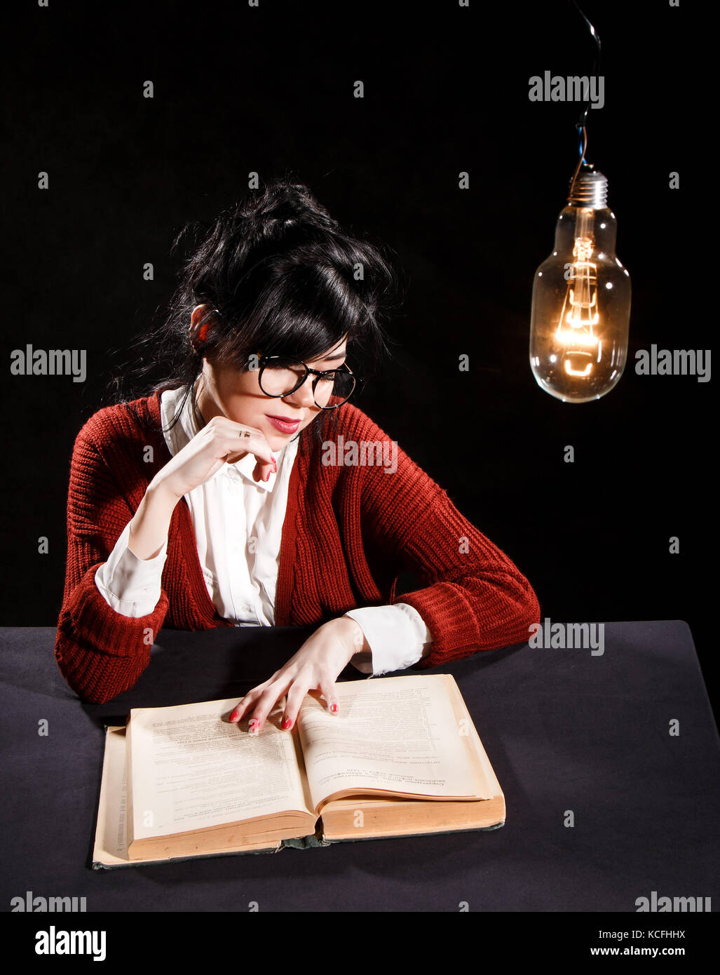 Pretty young woman reading under the light bulb Stock Photo