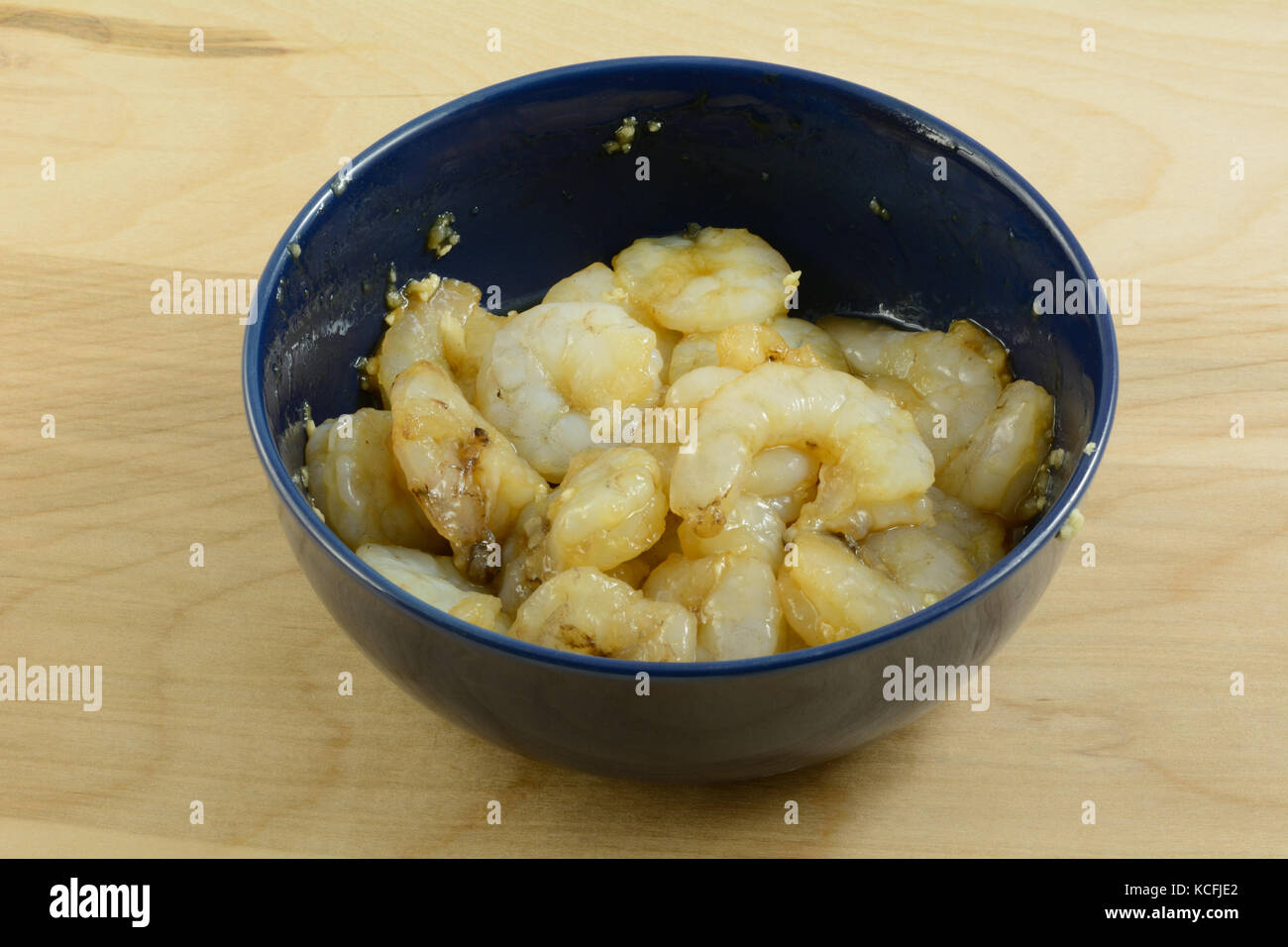 Raw shrimp marinating in hoisin sauce with ginger and minced garlic in bowl before cooking Stock Photo