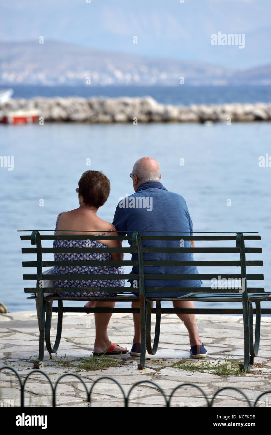 an older couple or a couple sitting on a bench looking out to sea with ...