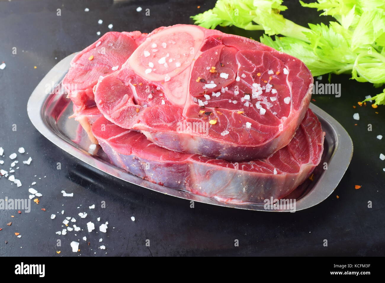 Raw veal meat with bone. Ossobuco meat on a metal tray on a grey abstract background with some green fresh celery leaves. Italian traditional food Stock Photo