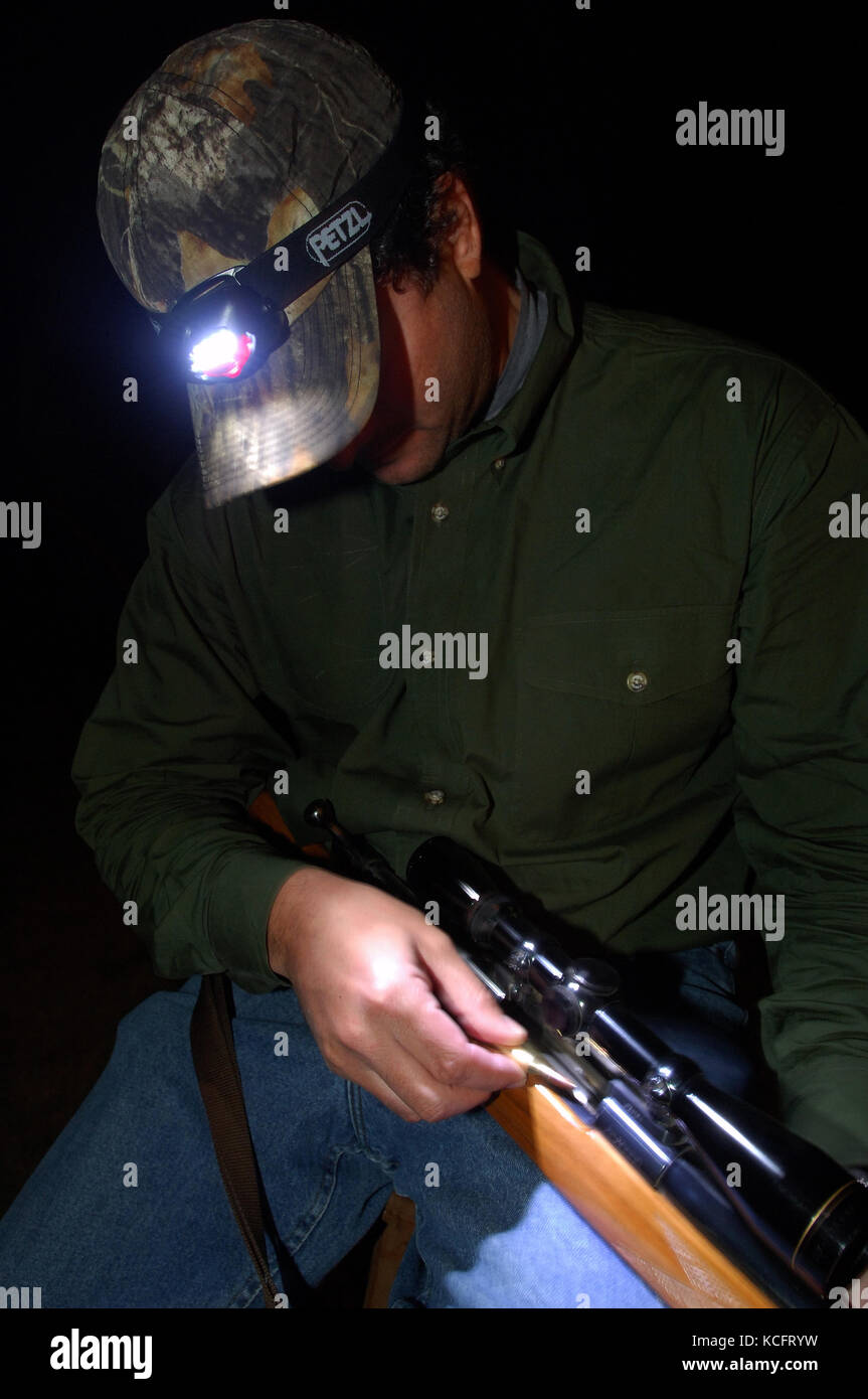 A deer hunter in Texas loads his hunting rifle with the aid of a headlamp Stock Photo