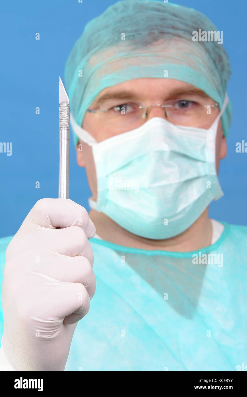 Surgeon holding scalpel up his face over blue background Stock Photo