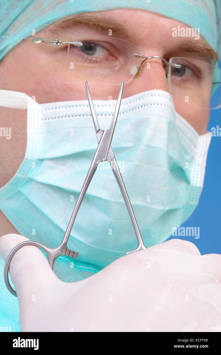 Surgeon holding curved forcept up his face over blue background Stock Photo