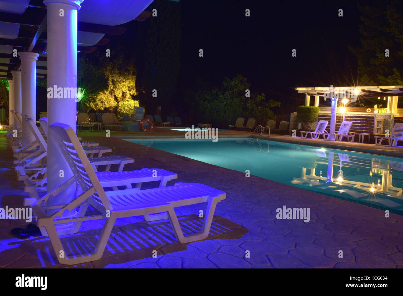 sunbeds and loungers next to a swimming pool in the dark with mood