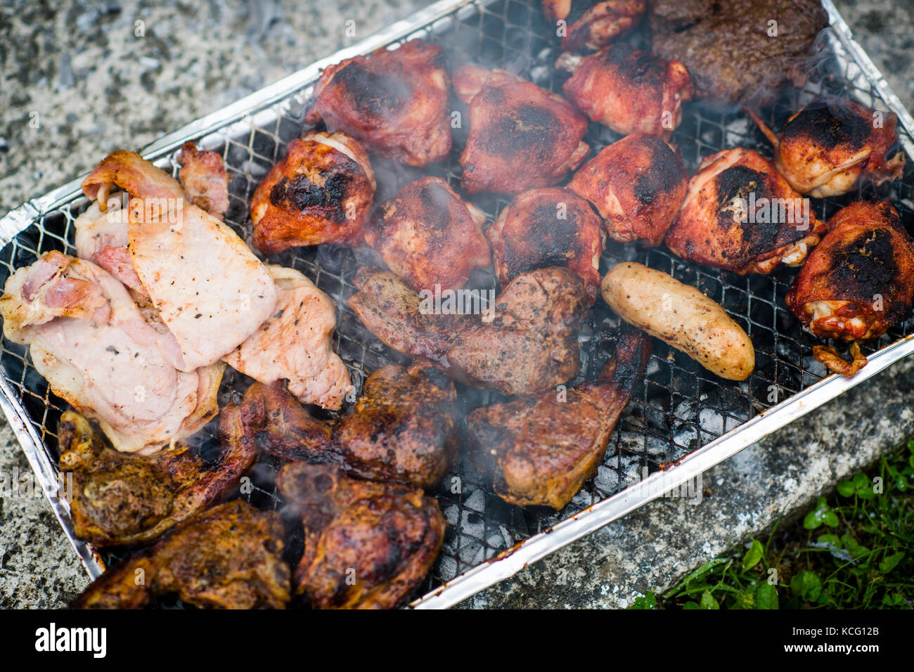 Meat (lamb chops, chicken thighs, sausage,  bacon) cooking on a disposable barbecue, UK Stock Photo