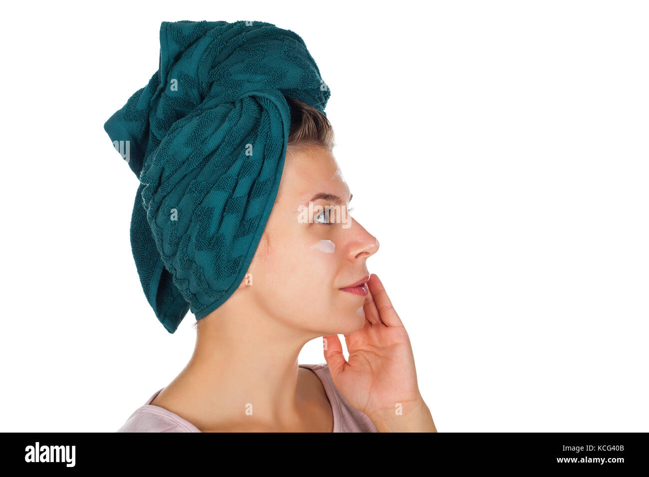 Young woman applying face moisturizer after shower, wearing a towel on