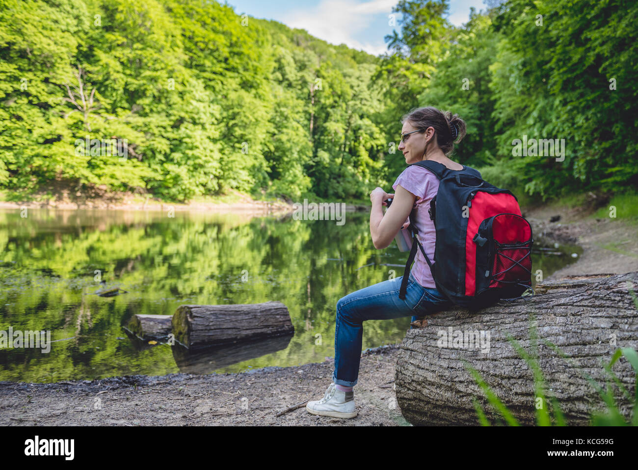 Woman sitting on a tree log by the lake and holding water bottle Stock ...