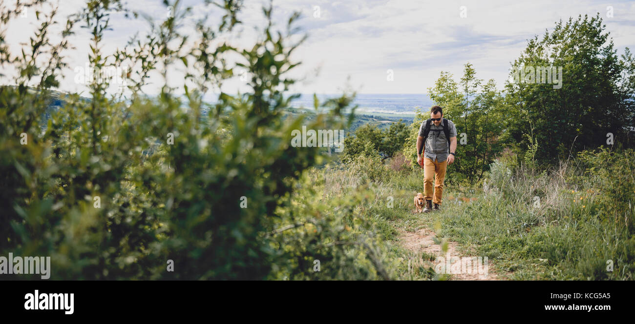 Man with a dog walking along a hiking trail on the mountain Stock Photo