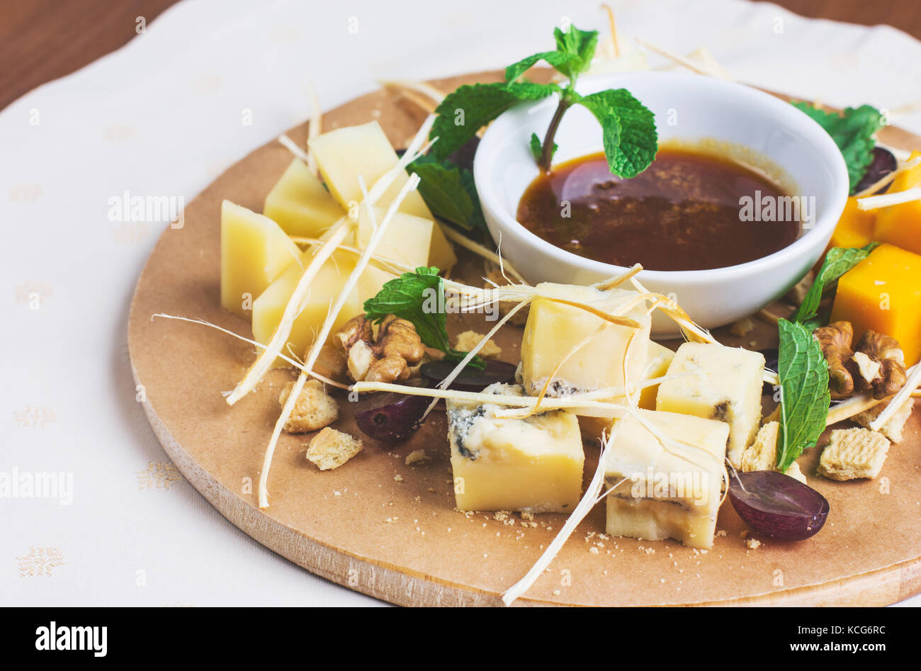 Different types of cheese with honey, nuts and fruits on round wooden