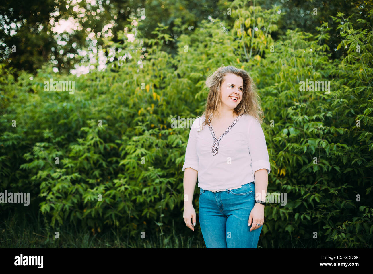 Young Beautiful Pretty Plus Size Caucasian Girl Woman Dressed In White Blouse And Blue Jeans Enjoying Life And Smiling Standing On Summer Green Forest Stock Photo