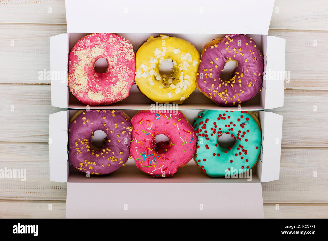 Colorful donuts in the cardboard box on the white wooden background Stock Photo