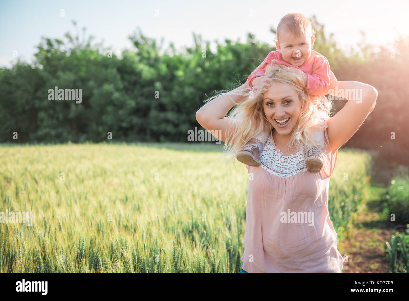 Mother Carrying Baby Daughter Piggyback and standing by the wheat field Stock Photo
