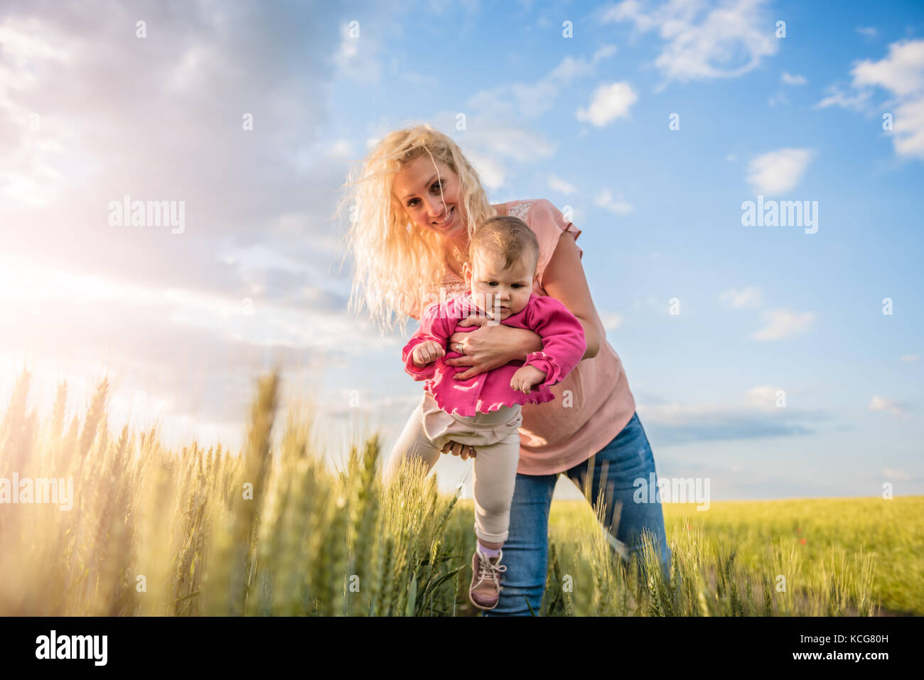 Happy mother holding her baby girl her arms in the wheat field Stock Photo