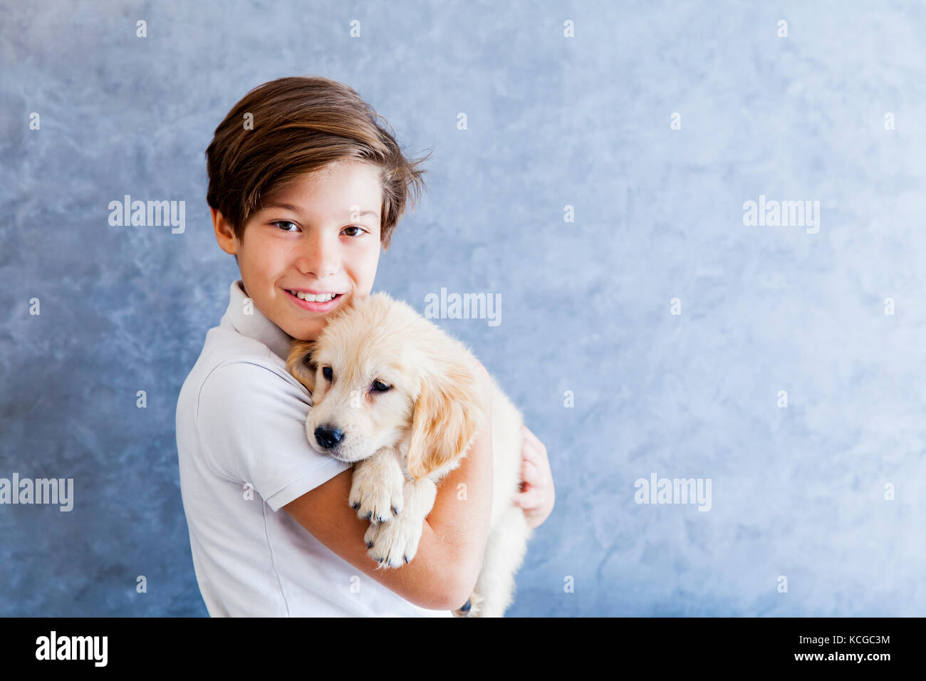 Teenage boy holding  the golden retriever baby dog by the wall Stock Photo