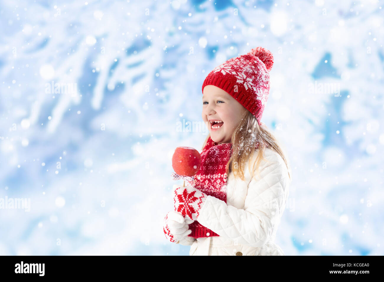 Child eating candy apple on winter fair. Kids eat toffee apples on Christmas market in snow. Outdoor fun on snowy day. Family vacation in Xmas season. Stock Photo