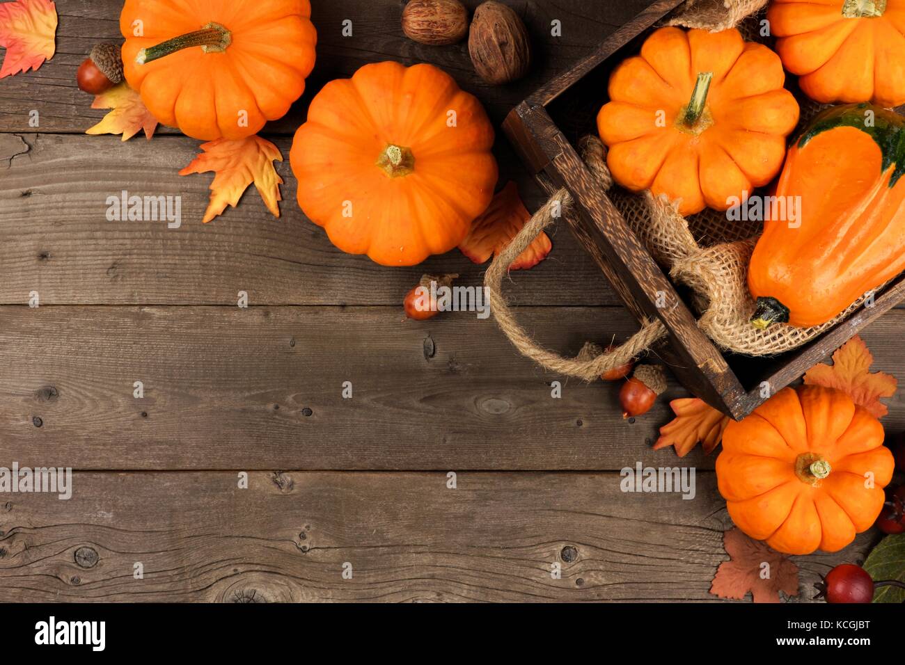 Autumn corner arrangement of leaves and a crate of pumpkins over a rustic wood background Stock Photo