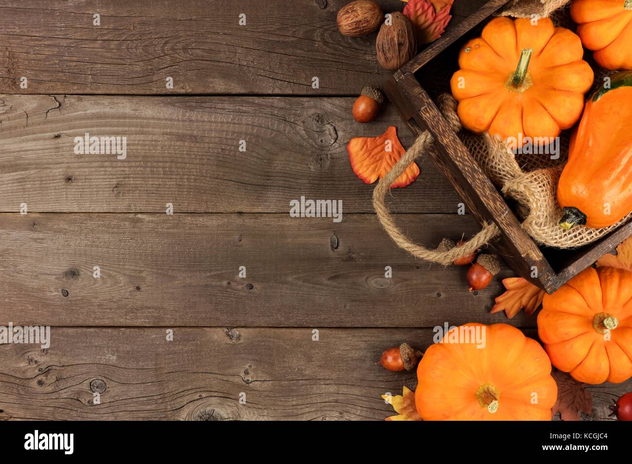 Autumn side arrangement of leaves and a crate of pumpkins over a rustic wood background Stock Photo