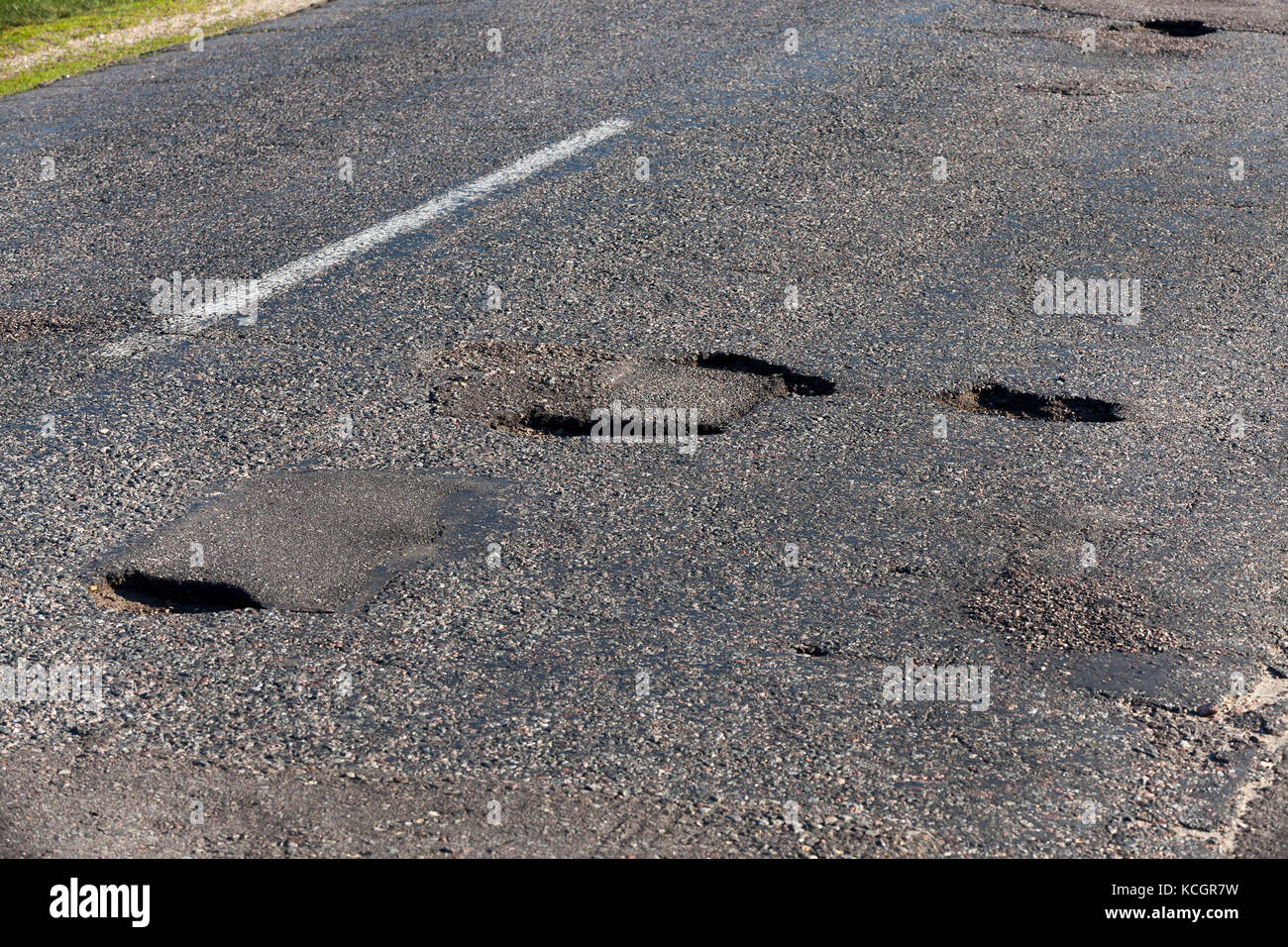 A large number of holes in the asphalt road. Poor quality of construction and infrastructure in the countryside. photo close up Stock Photo