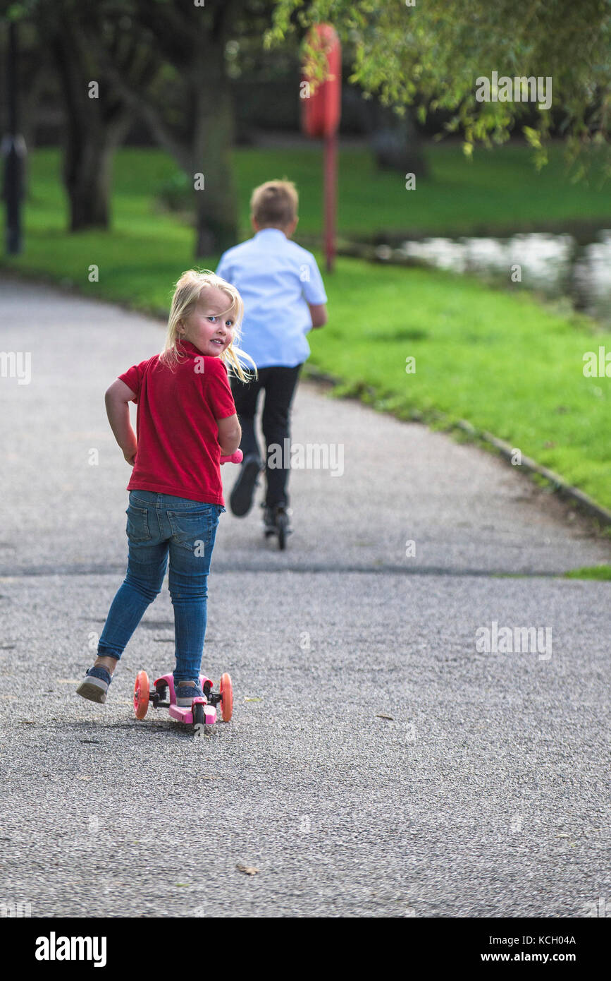 Children riding scooters - two children having fun riding their scooters along a path. Stock Photo