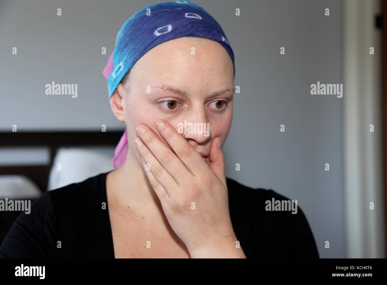 Young cancer patient in a headscarf holds head in hands with stress Stock Photo