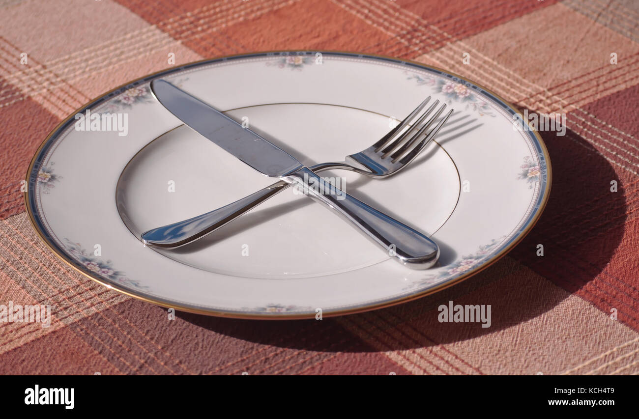 A fall place setting with a knife and fork crossed on the plate on a plaid table cloth Stock Photo