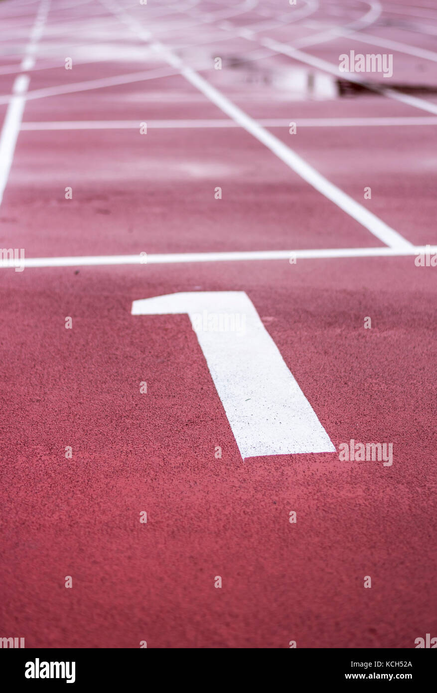 A white painted number one at the start line on a red running track. Stock Photo