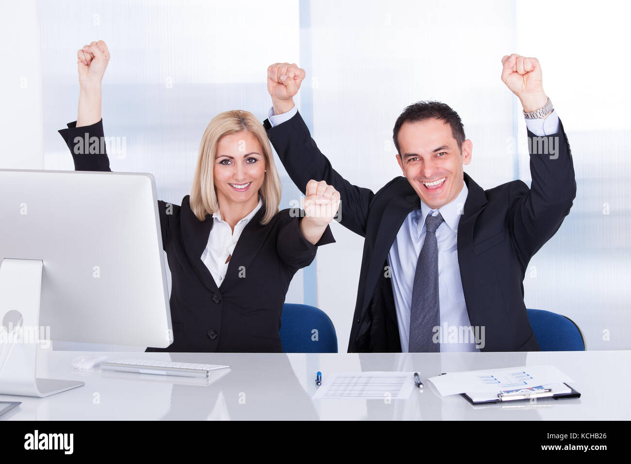 Excited Businessman And Businesswoman Raising Hands At Office Stock Photo