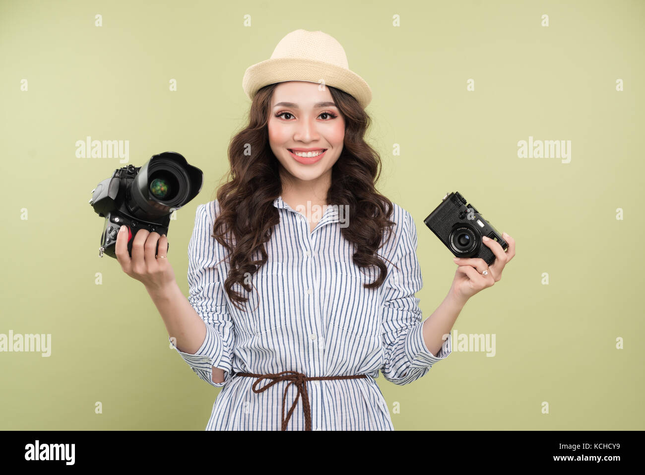 Young asian woman comparing professional and compact cameras on green background Stock Photo
