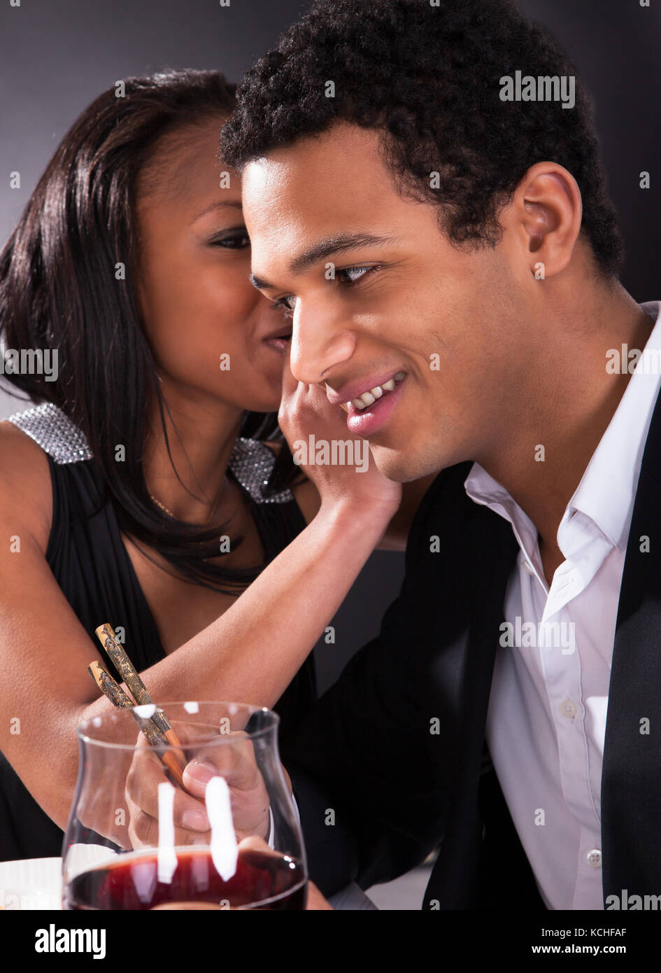 Portrait Of Woman Whispering To Boyfriend's Ear At Dinner Stock Photo