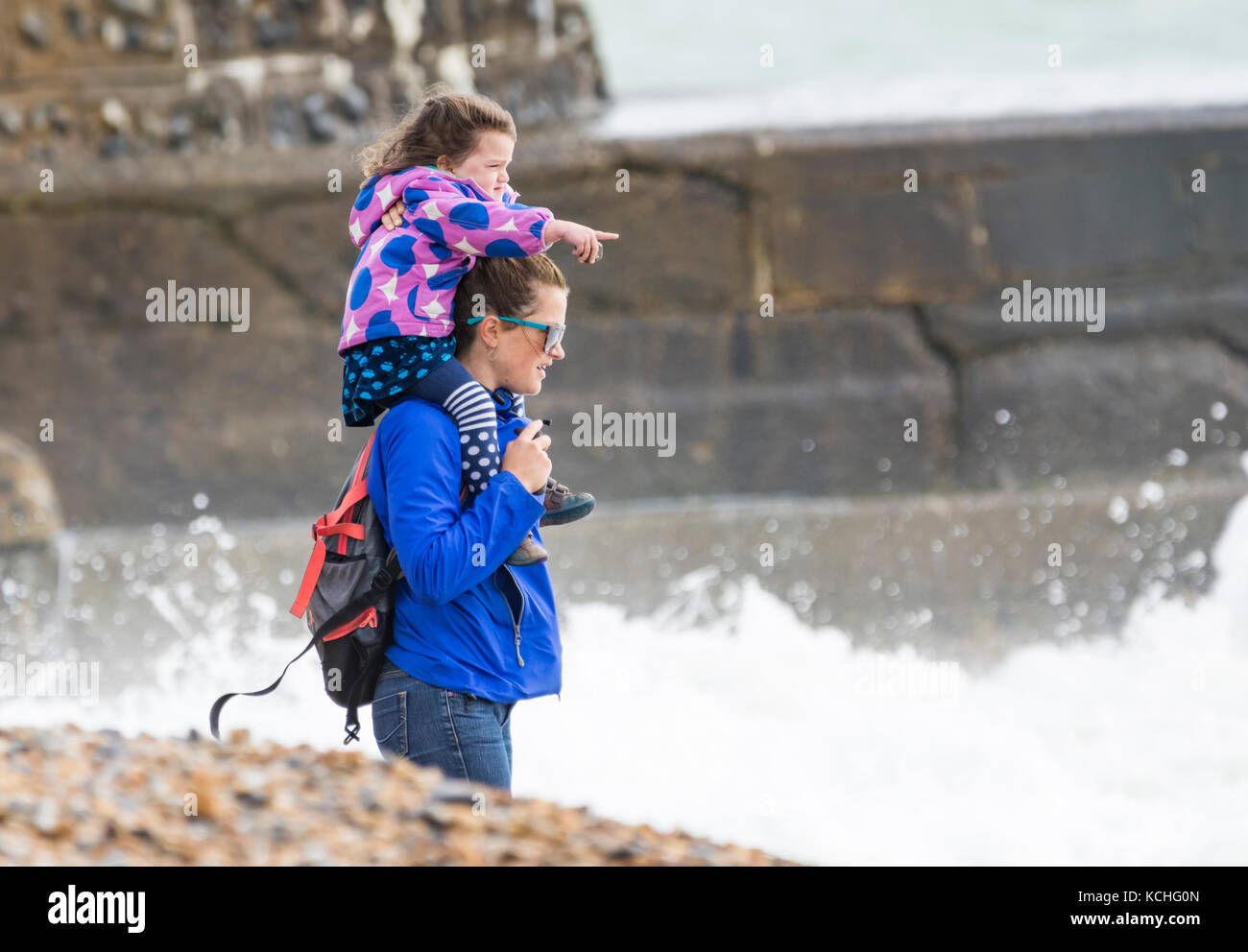 Young girl being carried on woman's shoulders (piggyback ride) on a beach in poor windy weather in Autumn, in Brighton, East Sussex, England, UK. Stock Photo