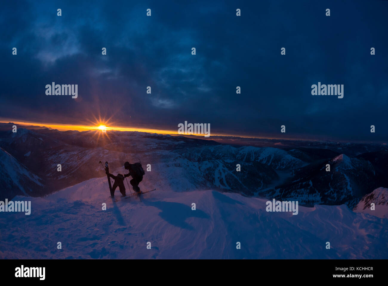 Two backcountry skiers on the summit of Ymir Peak at sunset, Nelson, British Columbia Stock Photo