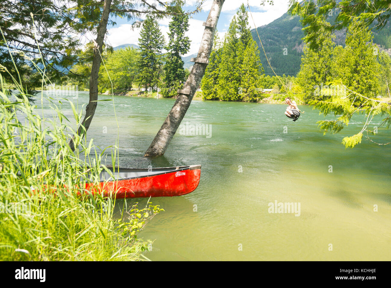 A man takes a daring rope swing on a pull-over of the Slocan River, British Columbia Stock Photo