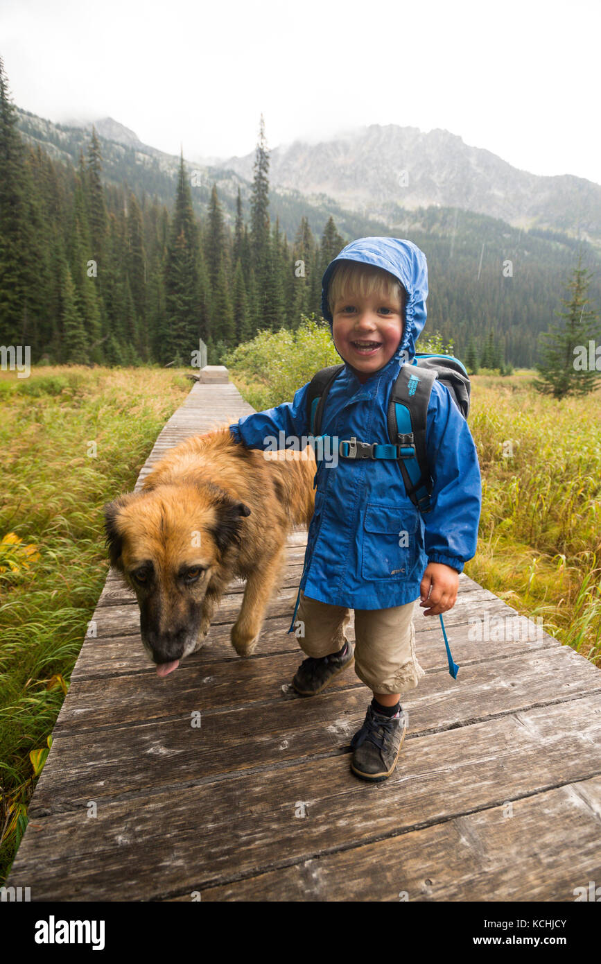 A happy toddler (boy) and his dog hikes on a boardwalk around Gibson Lake in Kokanee Glacier Provincial Park, British Columbia Stock Photo
