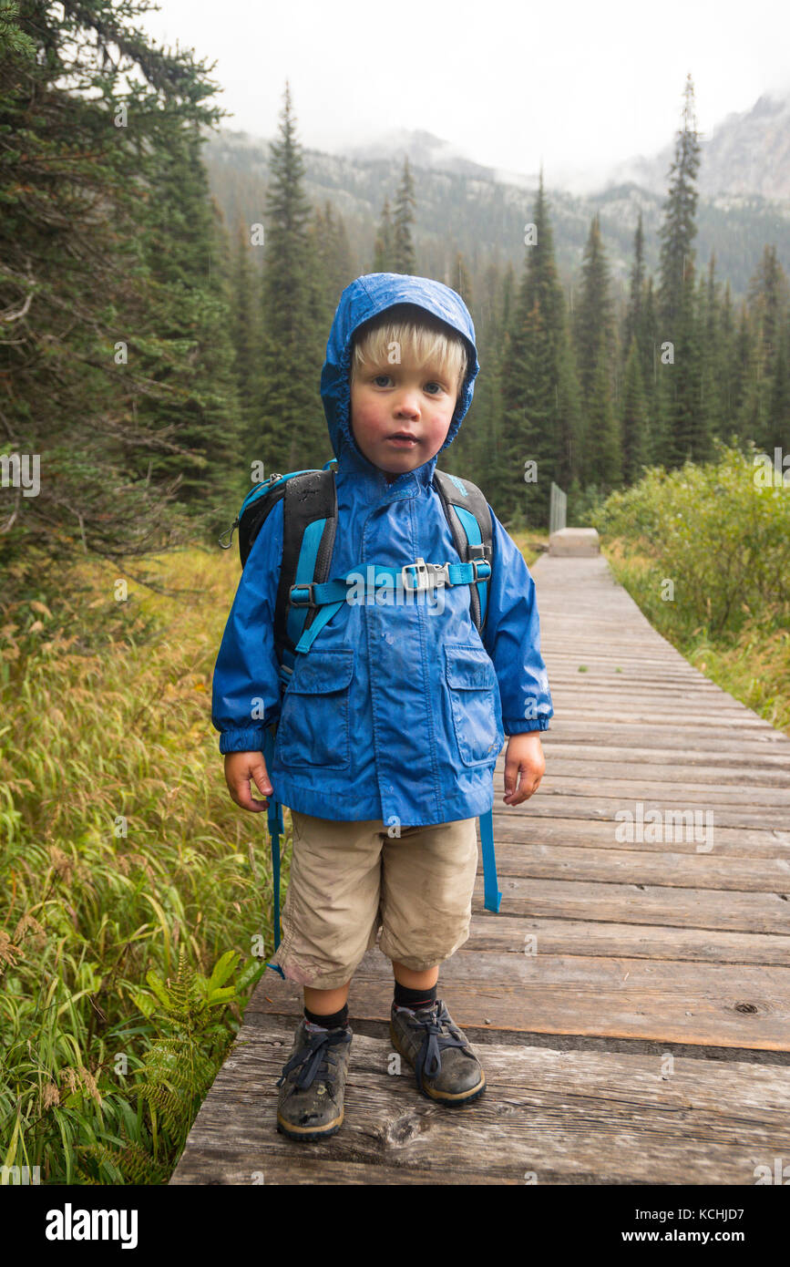 A toddler (boy) poses on a rainy boardwalk around Gibson Lake in Kokanee Glacier Provincial Park, British Columbia Stock Photo