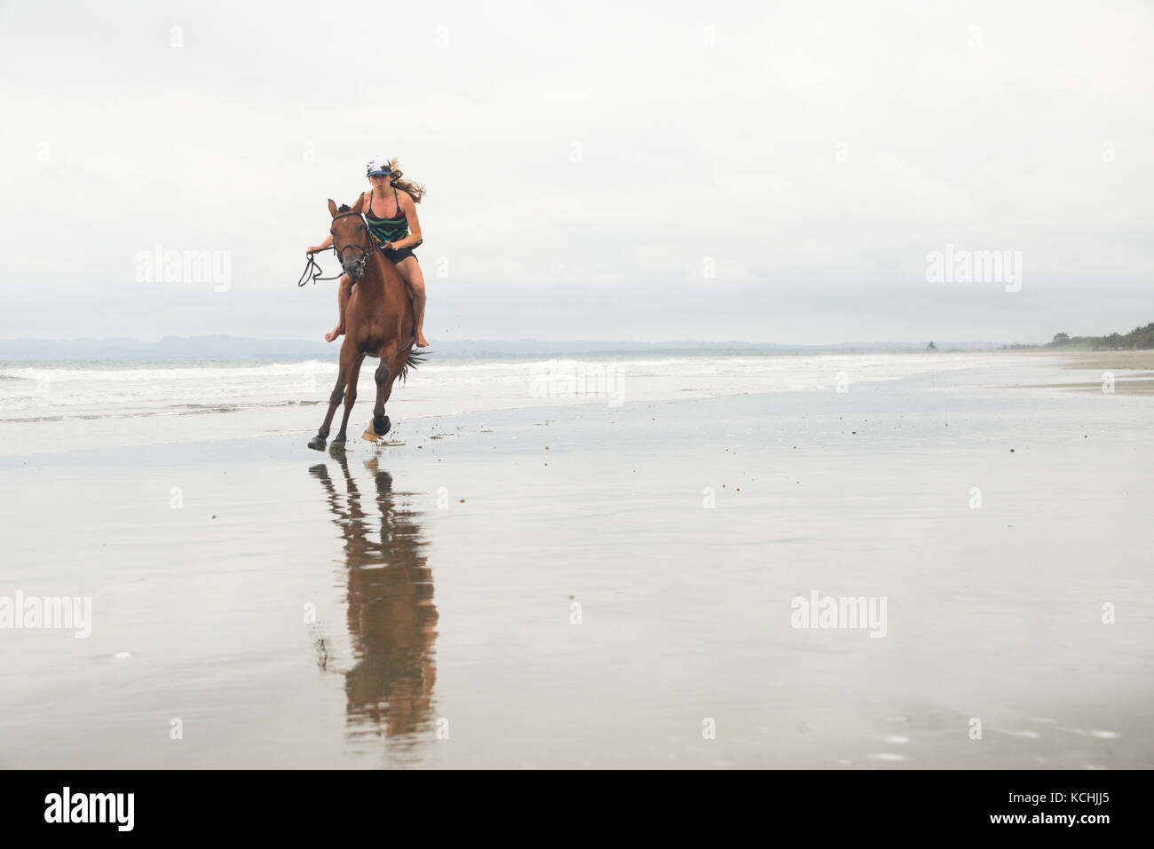 A woman gallops a horse on a beach in Ecuador Stock Photo