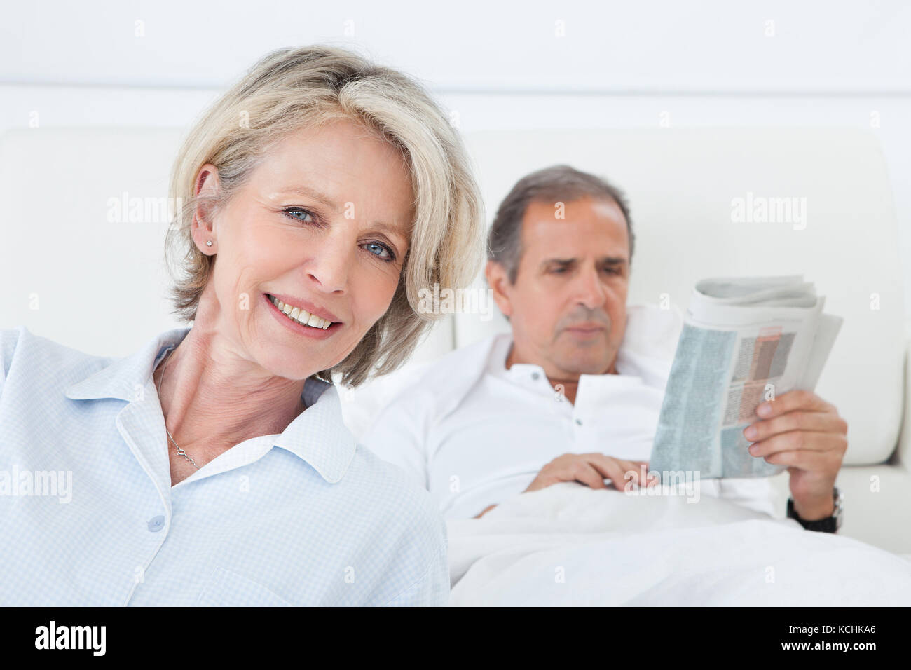 Happy Mature Woman Sitting In Front Of Man Reading Newspaper Stock Photo