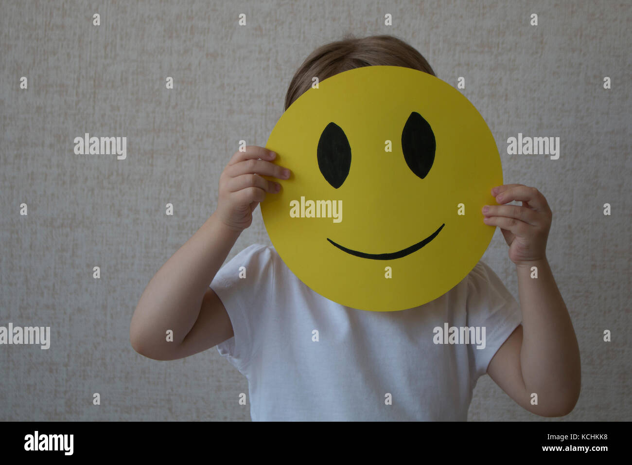 A kid holding a yellow circle with smile face emoticon instead of head. Stock Photo