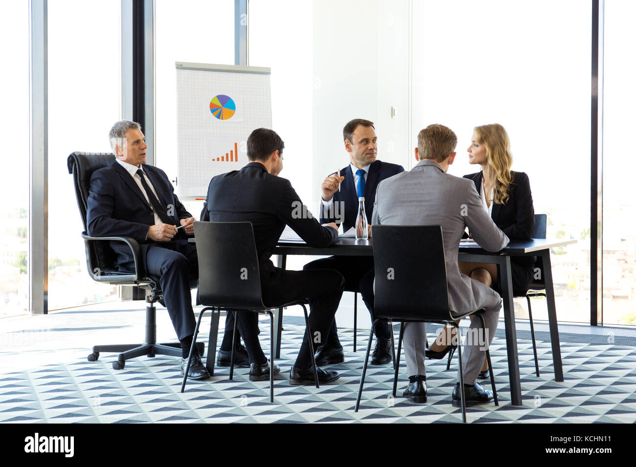 Business people sitting around meeting table, talking and working with