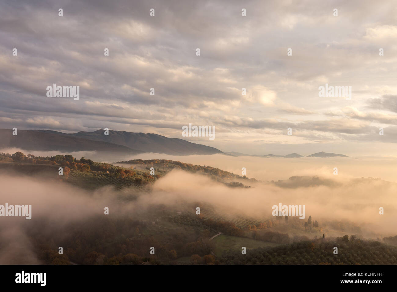 A valley in autumn filled by mist at sunset, with emerging hills and trees and beautiful warm, orange tones Stock Photo