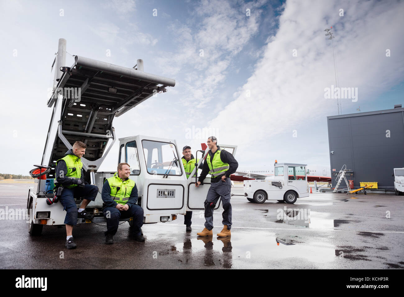 Happy male workers communicating at gangway on wet runway against sky Stock Photo