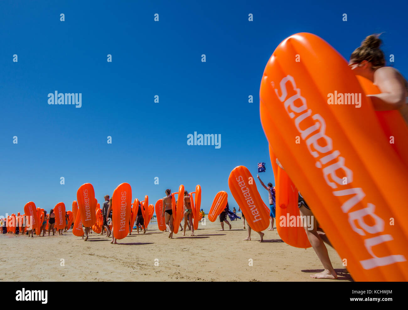 Beachgoers carrying inflatable Havianas flip flops into the surf