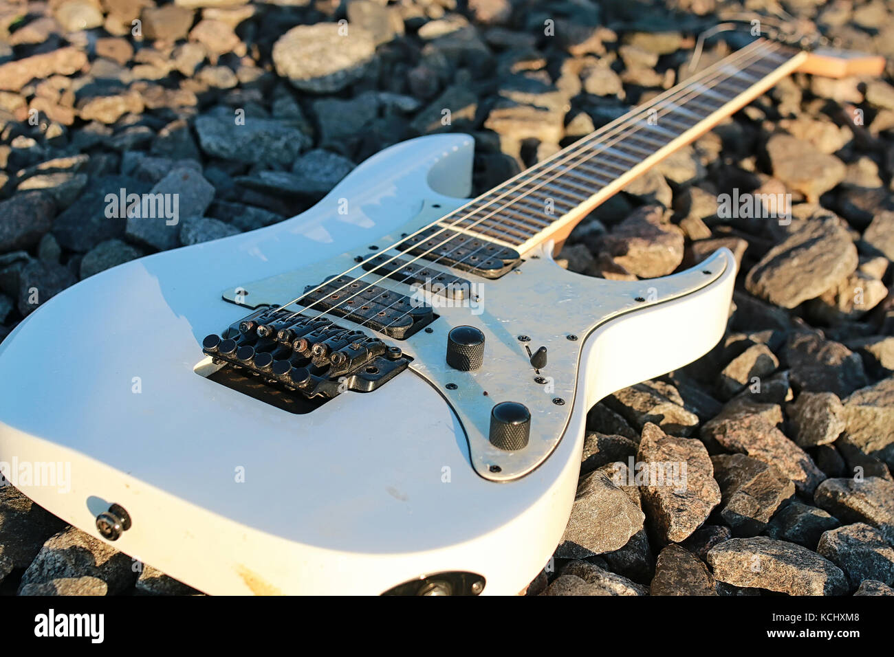 White Electric Guitar On The Railroad Tracks And Industrial Gray Stone white-electric-guitar-on-the-railroad-tracks-and-industrial-gray-stone