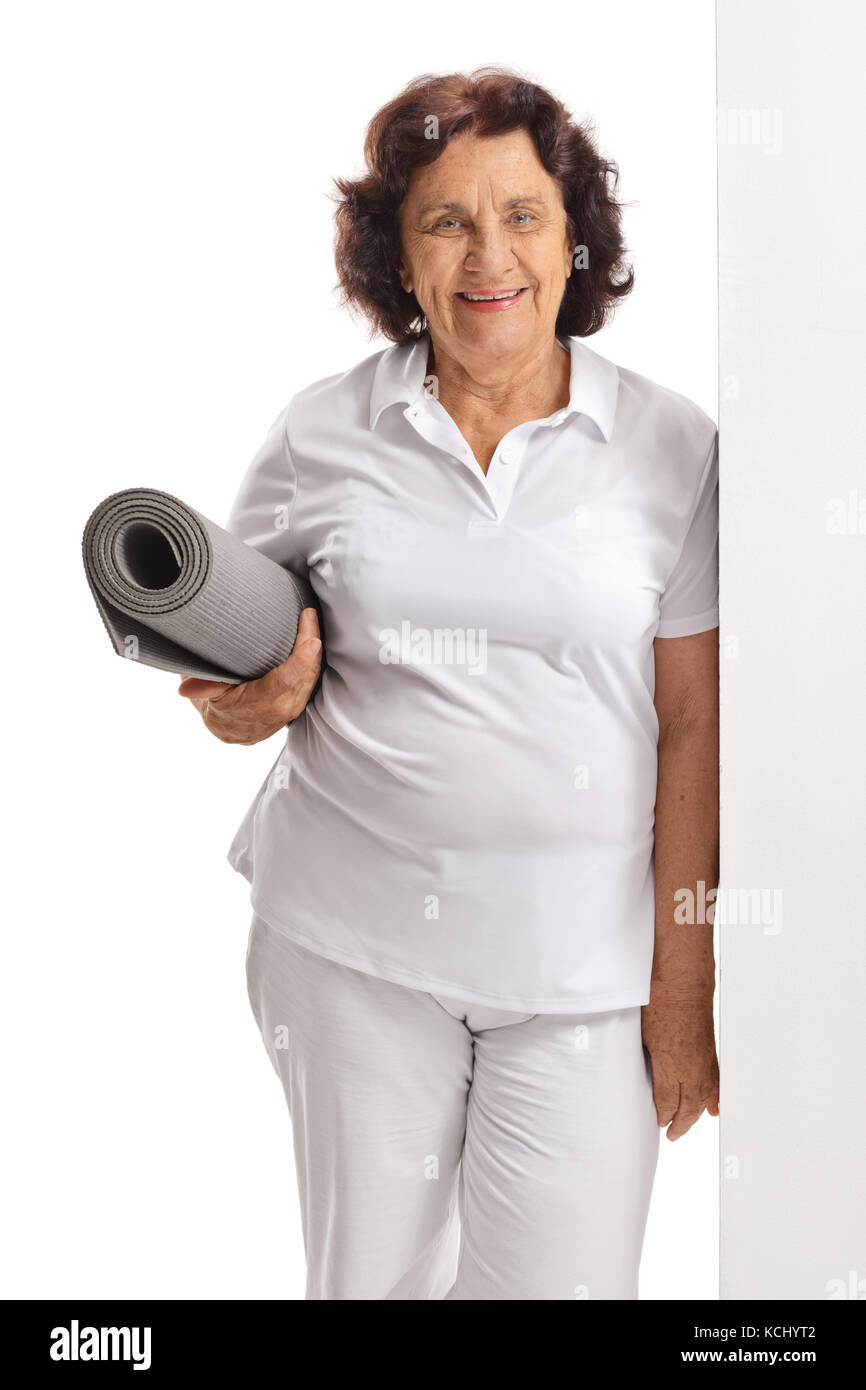 Elderly woman with an exercise mat leaning against a wall isolated on white background Stock Photo