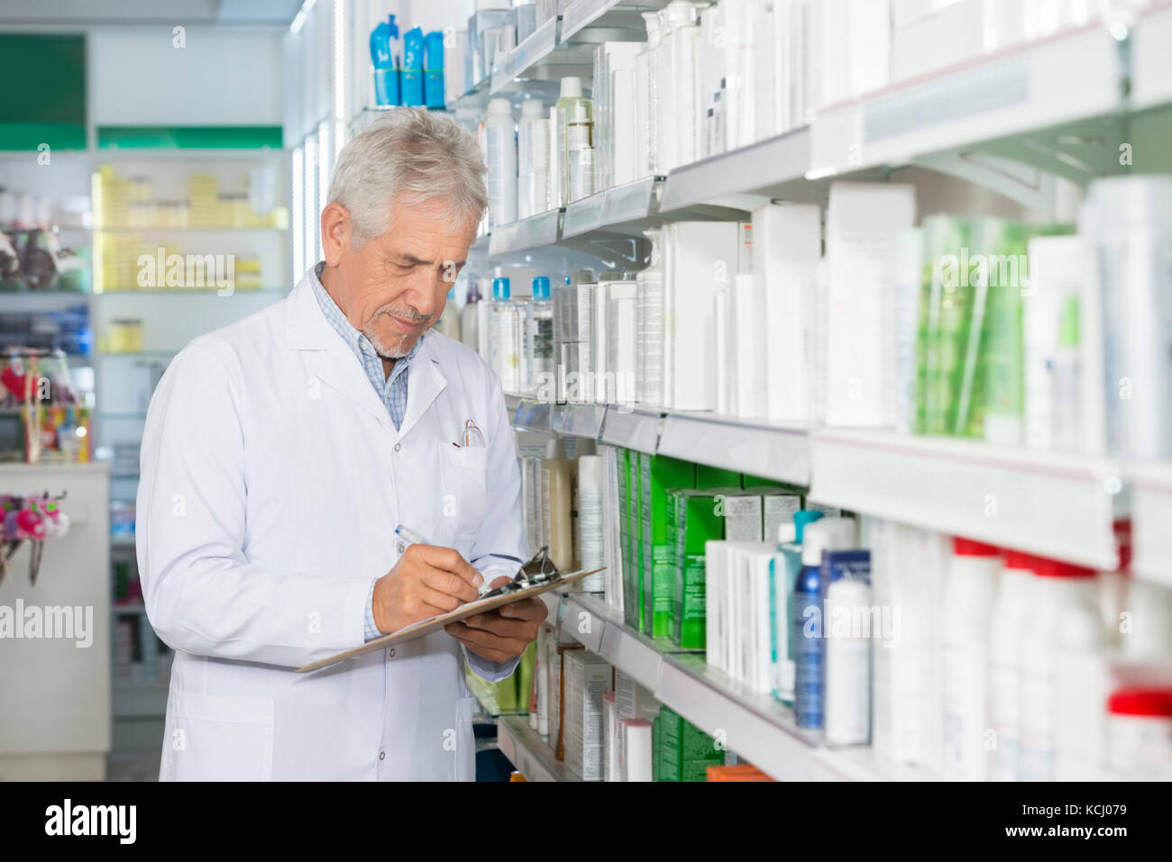 Chemist Writing On Clipboard While Standing By Shelves Stock Photo
