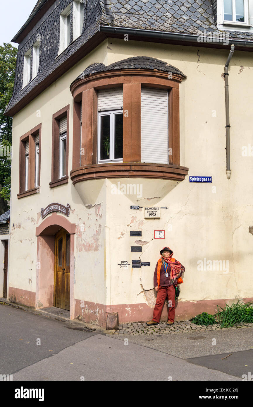 A woman in a hat next to high water (hochwasser) flood markers on a house wall,  Neumagen-Dhron, Mosel valley, Rheinland-Pfalz, Germany Stock Photo