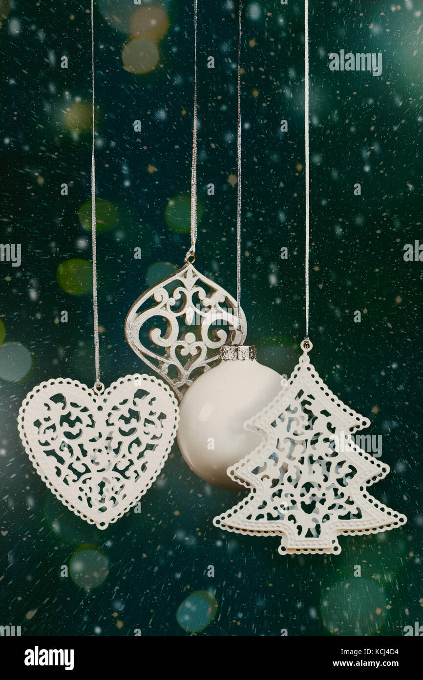 Christmas tree ornaments and balls hanging against a green background with snow, lights bokeh and sparks. Film grain added Stock Photo