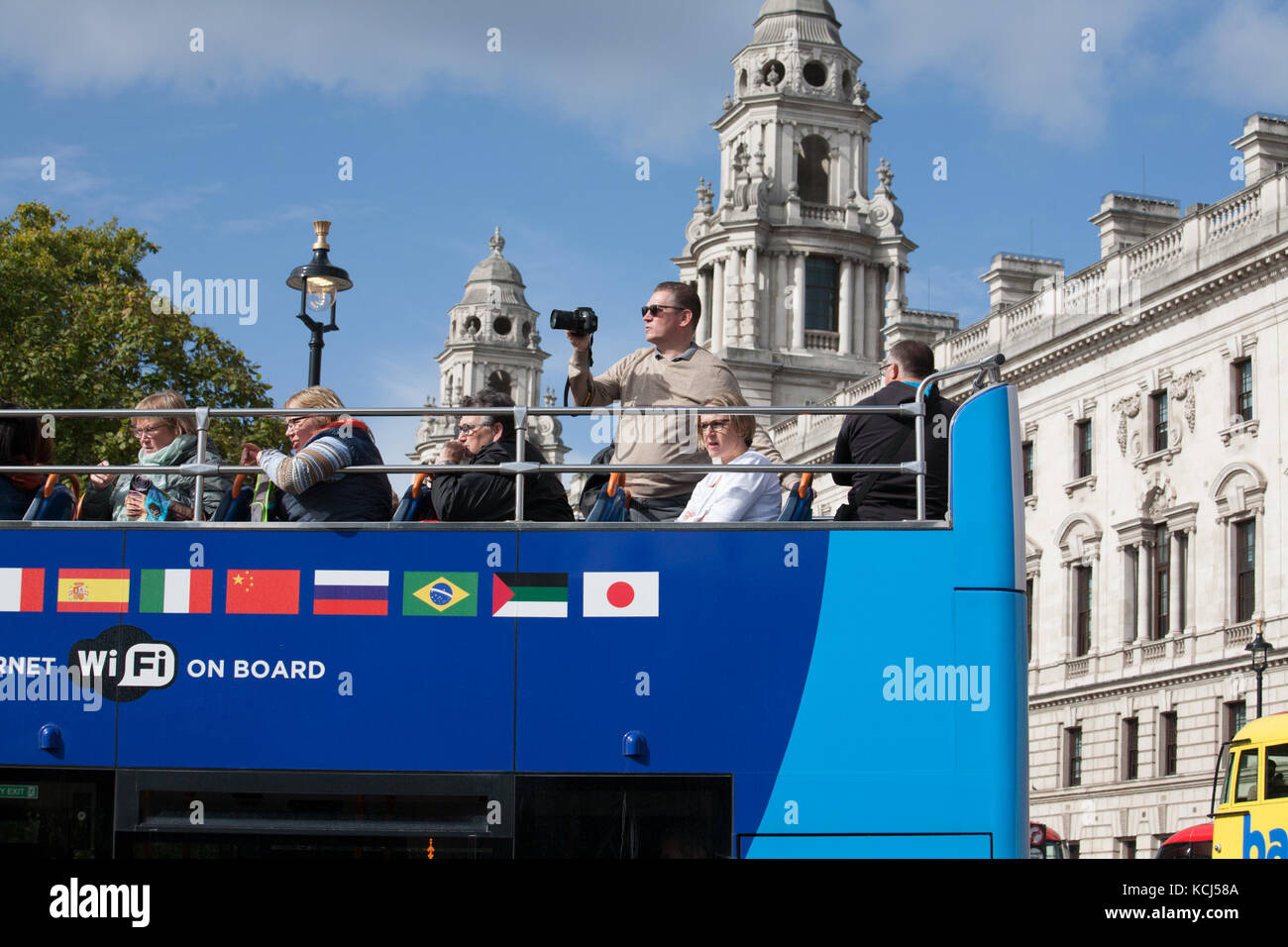 Tourist taking photographs on top deck of open top double decker London